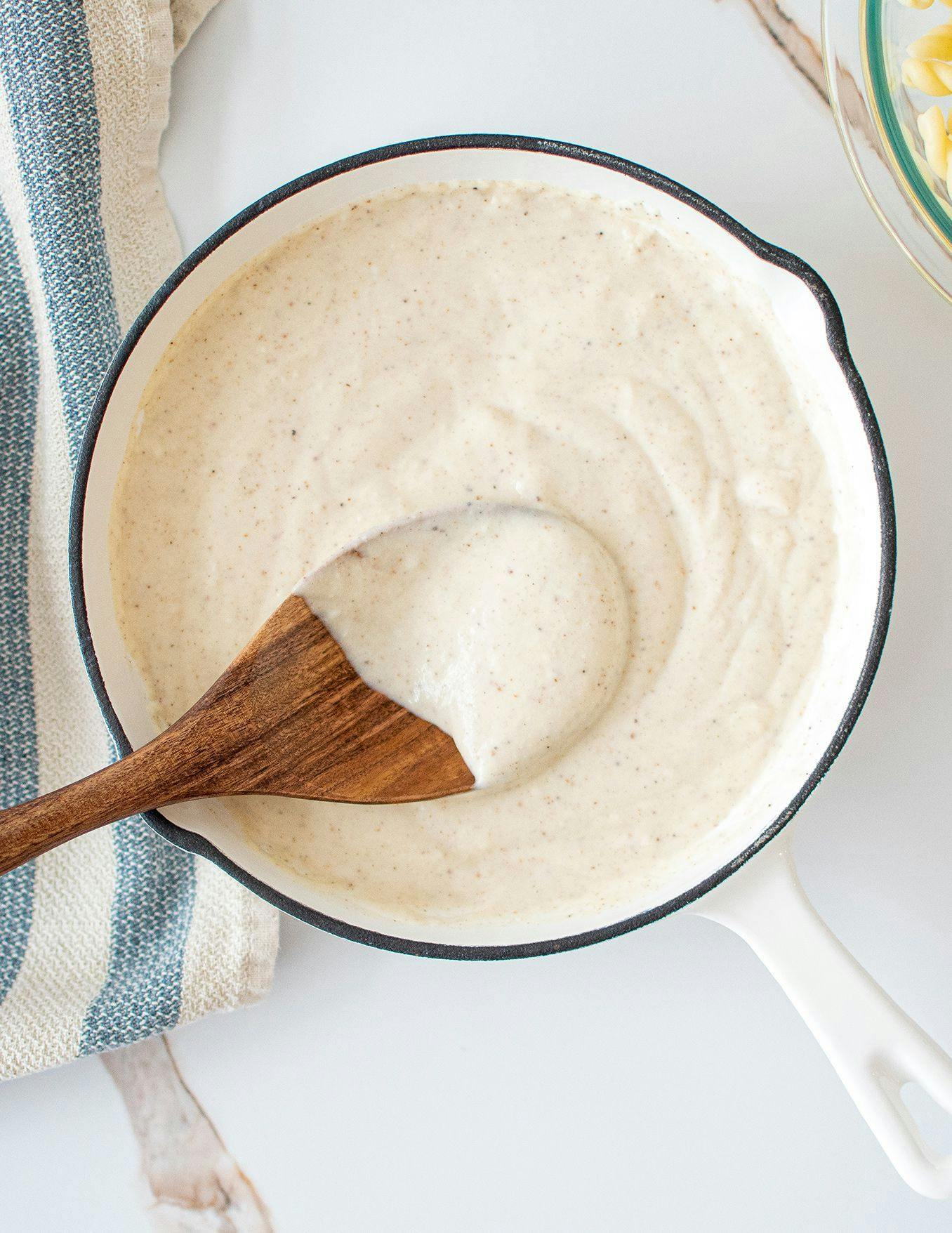 A bowl of creamy white sauce with a wooden spoon in it.