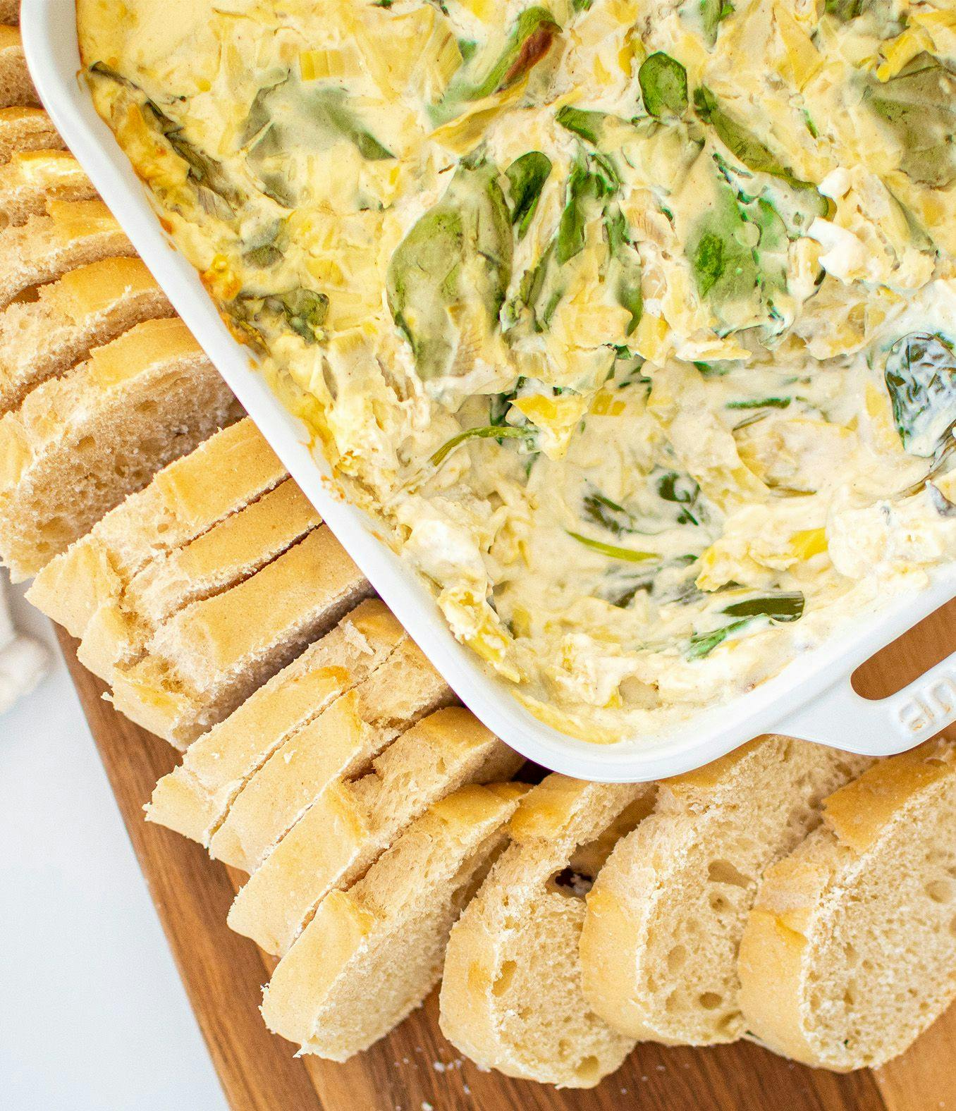 Spinach Artichoke Dip on a cutting board with bread.