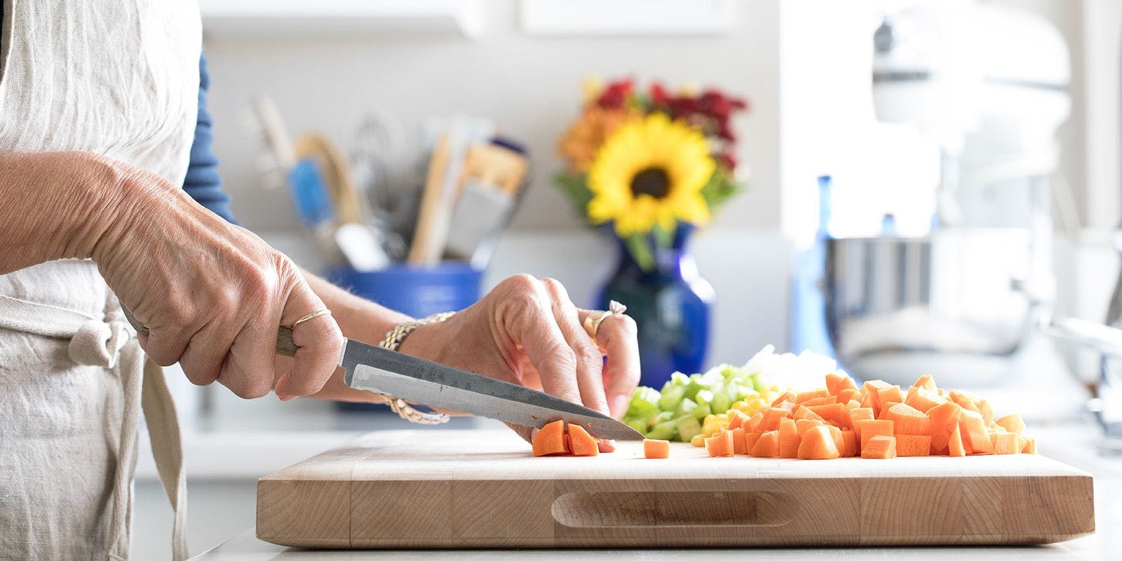 Carrots, celery and onions being chopped on wood cutting board.