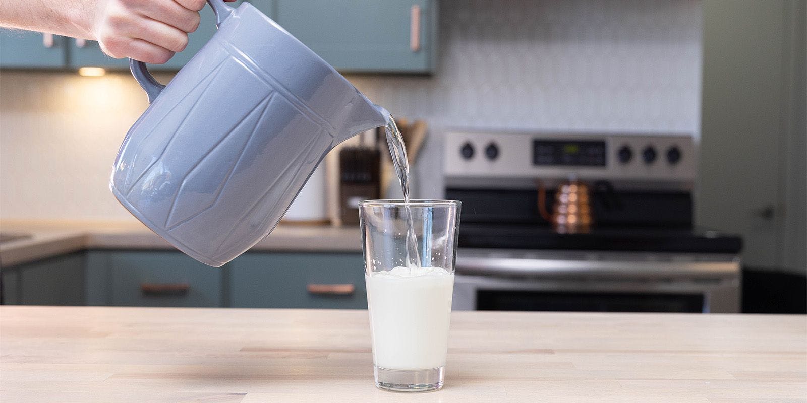 A man pours water from a pitcher into a glass of milk.