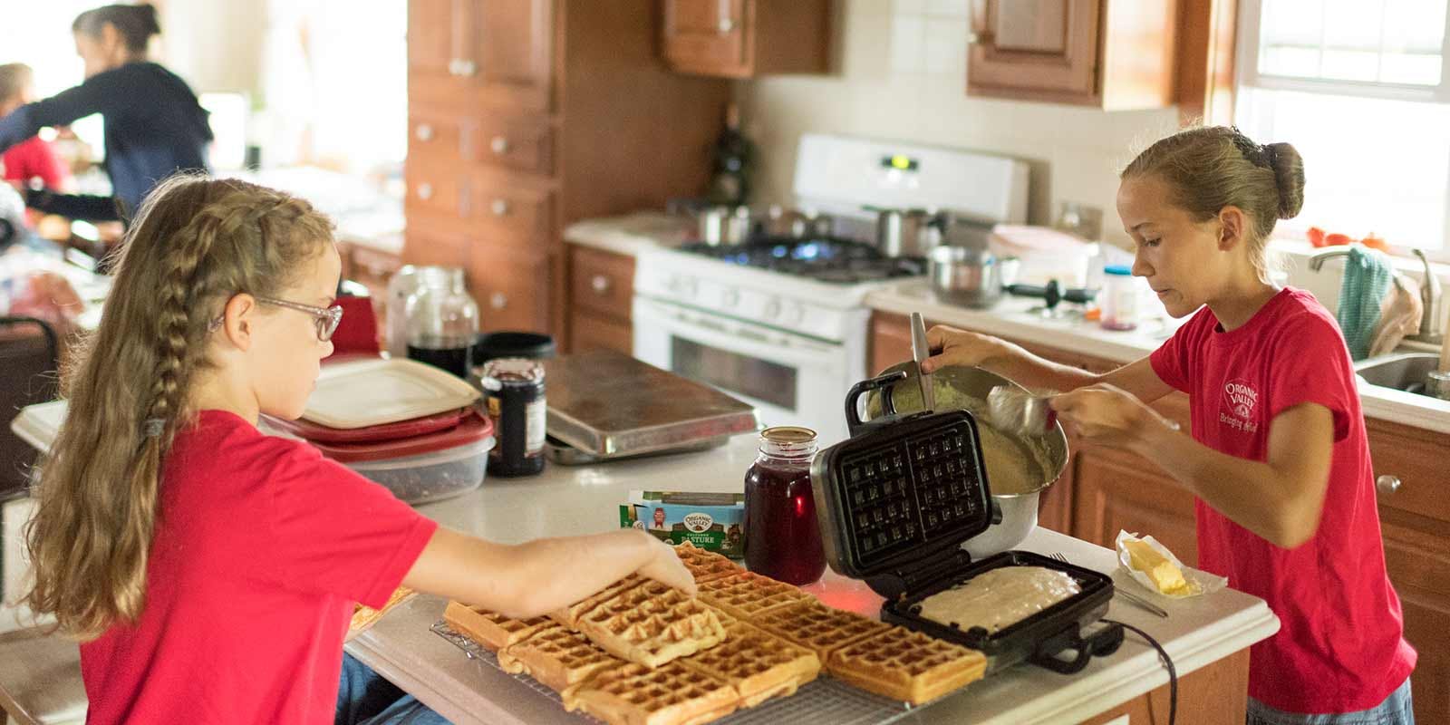 Two young girls make a large batch of waffles in their kitchen.