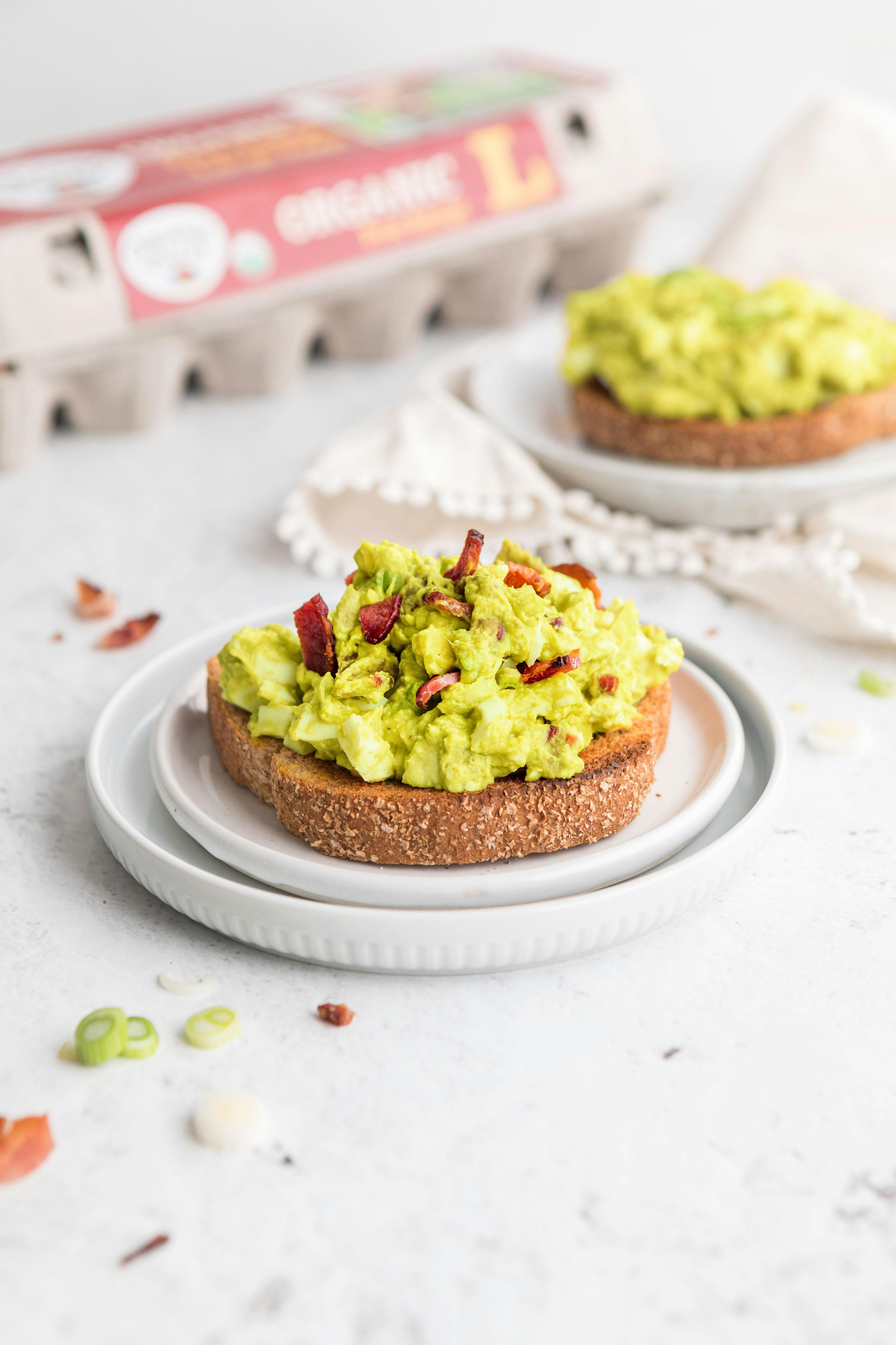 A piece of toast with Avocado Egg Salad with Bacon on top.