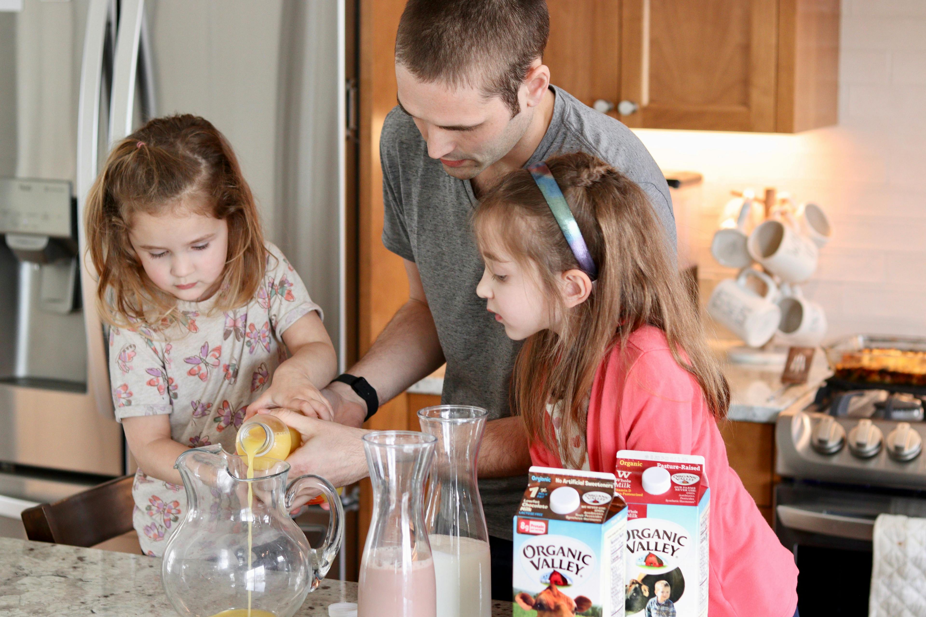 Dad helps his girls pour orange juice.