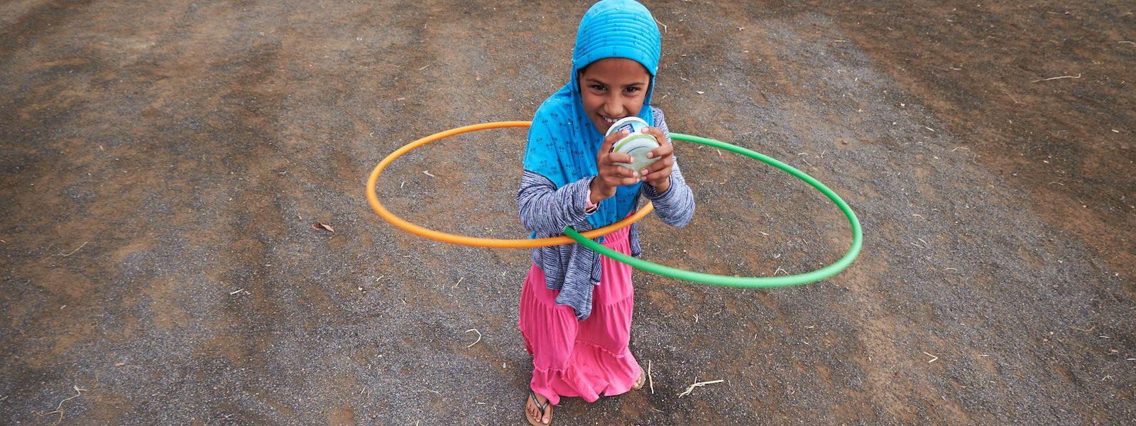 A girl shakes up a jar of butter while hula hooping.