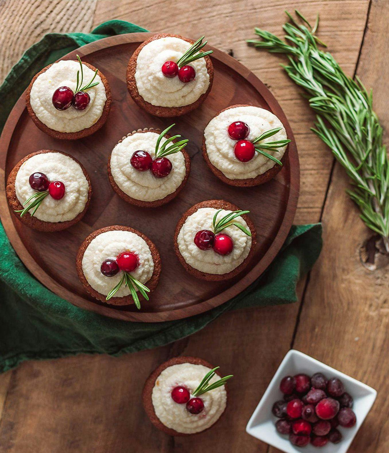 A plate of orange spice muffins next to a bowl of cranberries.