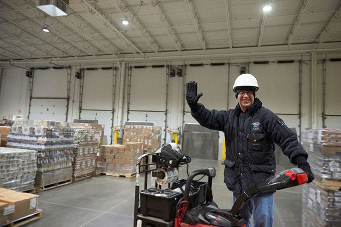 Man wearing hard hat driving fork lift waving.