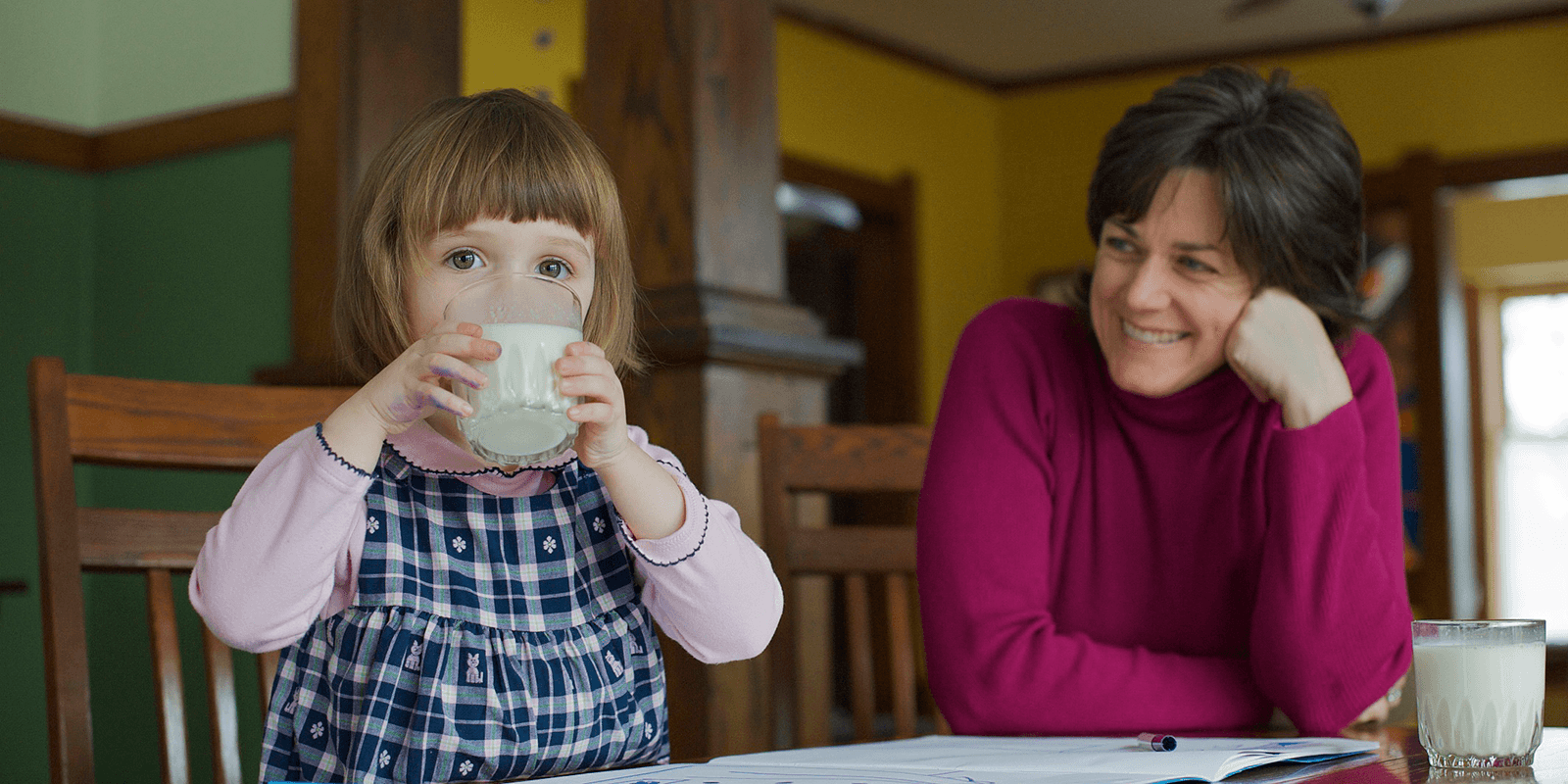 A girl drinks milk as her mom watches.