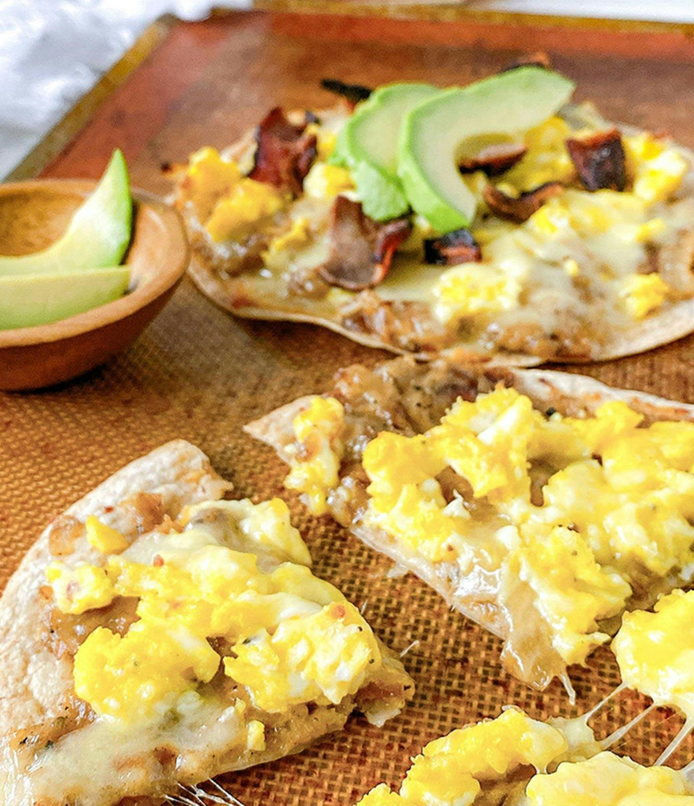 Breakfast pizza with avocado slices.