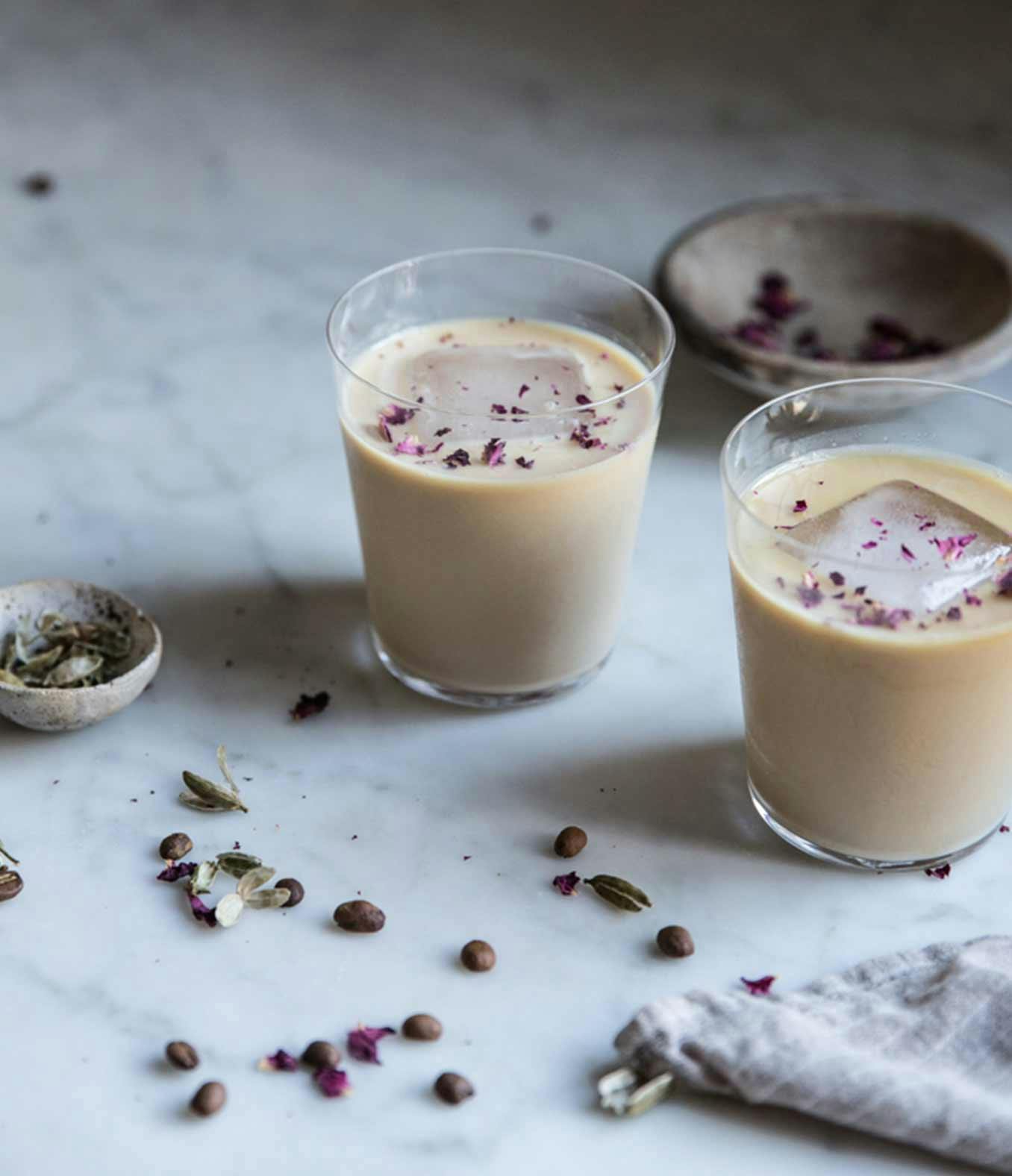 Cardamom Rose Lattes in two glasses with a large ice cube.