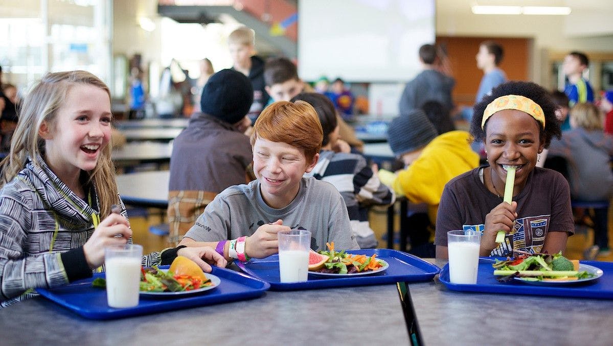 Children smile as they eat school lunch.