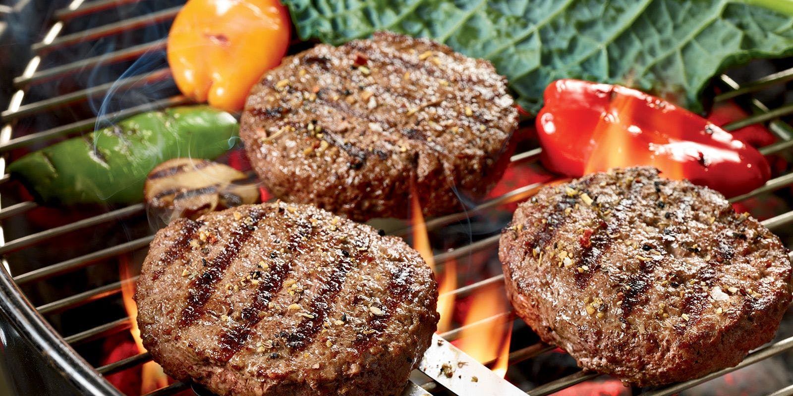 Hamburgers grilling on an open flame.