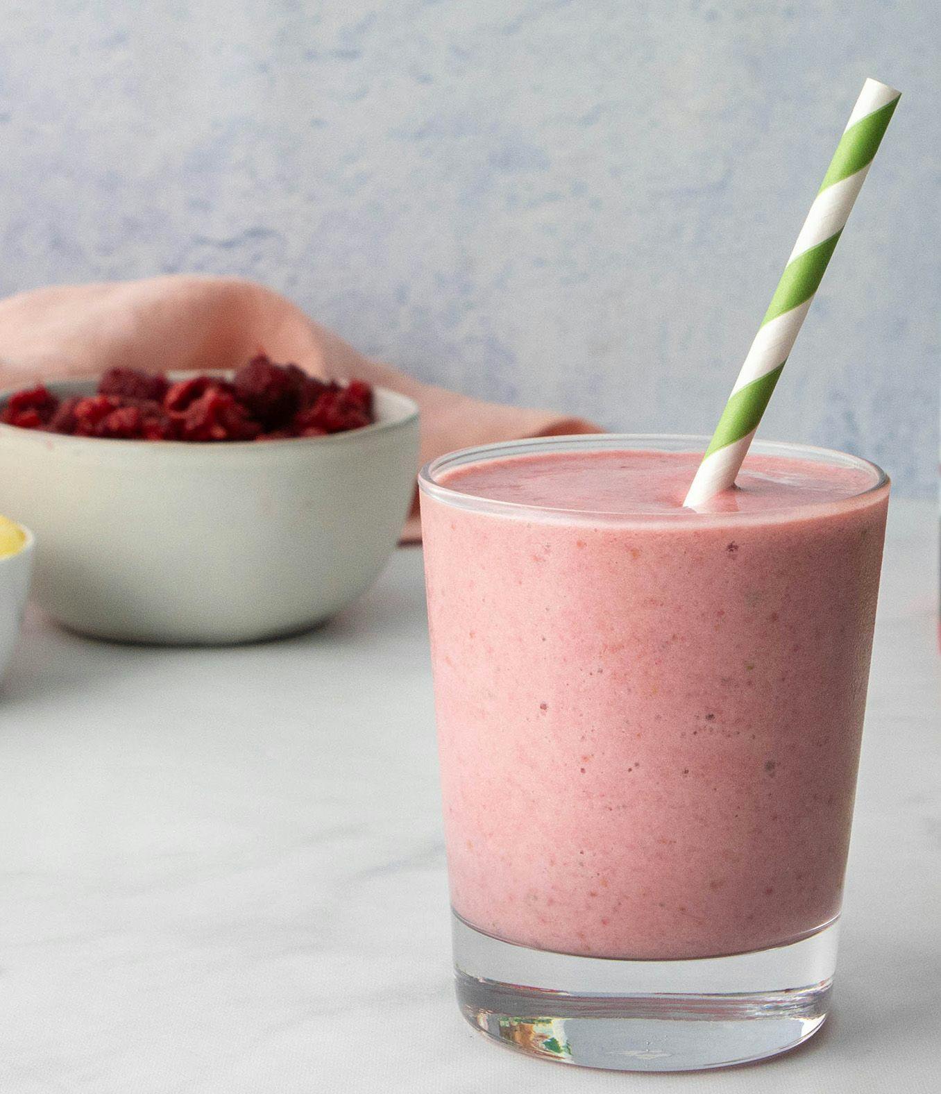 Smoothie with a green and white straw next to a bowl of fruit. 