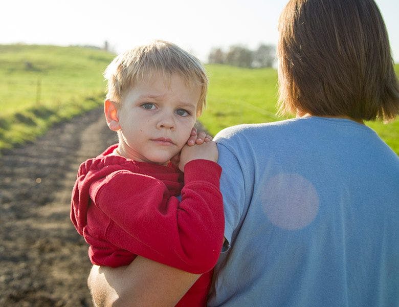 A farm mom holding her son while walking in the pasture lane.