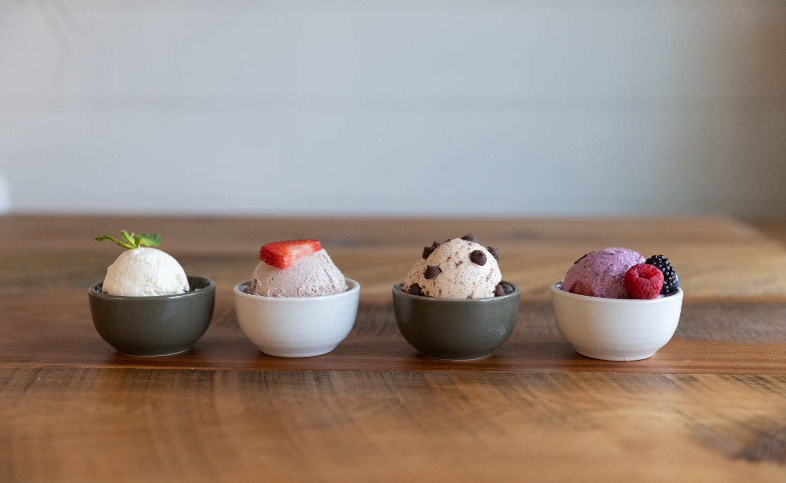 4 bowls of ice cream with varying toppings on a wooden table.