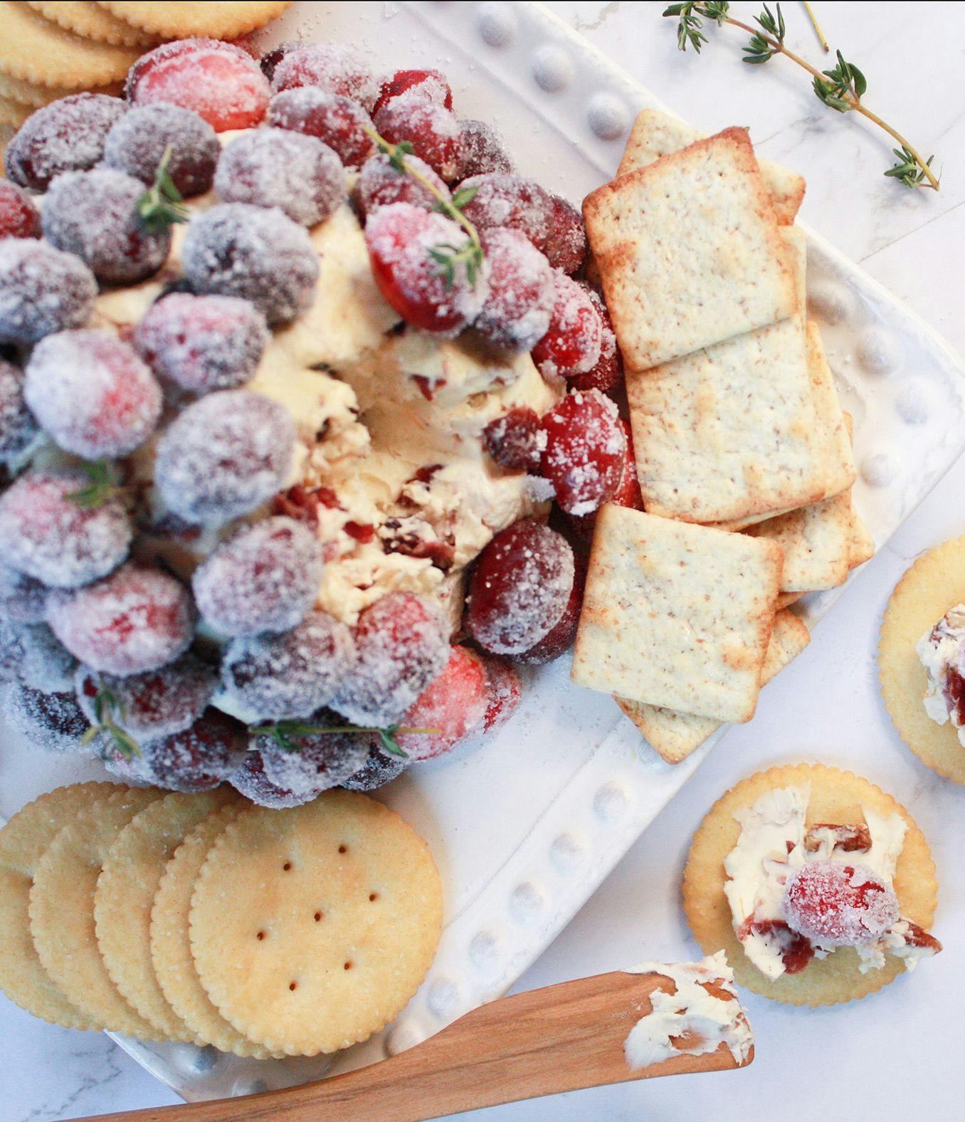 cheese ball with candied pecans and cranberries on a plate with crackers.