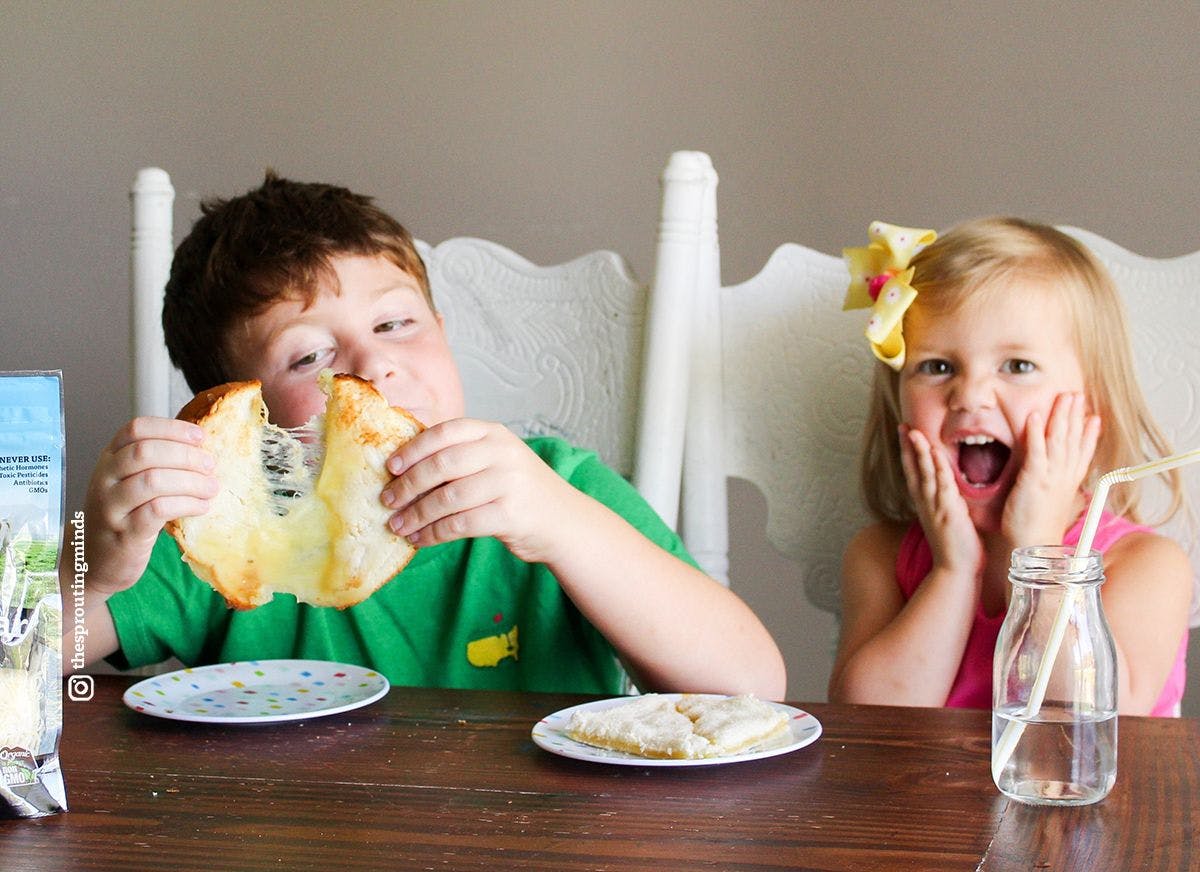 Kids sit at the table enjoying an organic grilled cheese sandwich with excited facial expressions.