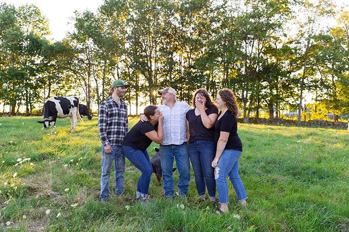 Farming family together on a cow pasture laughing and smiling.