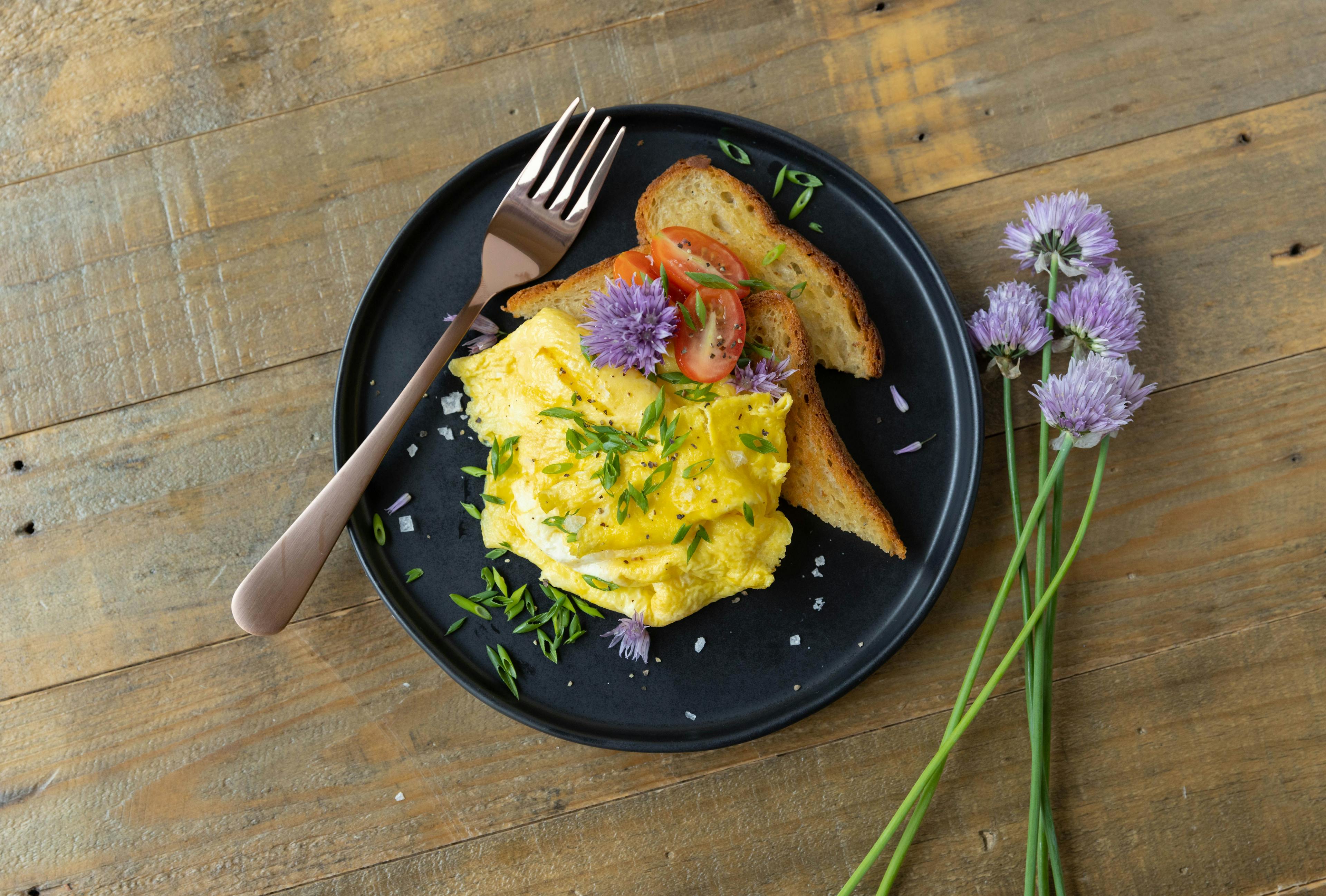 Chives on scrambled eggs with toast and tomatoes.