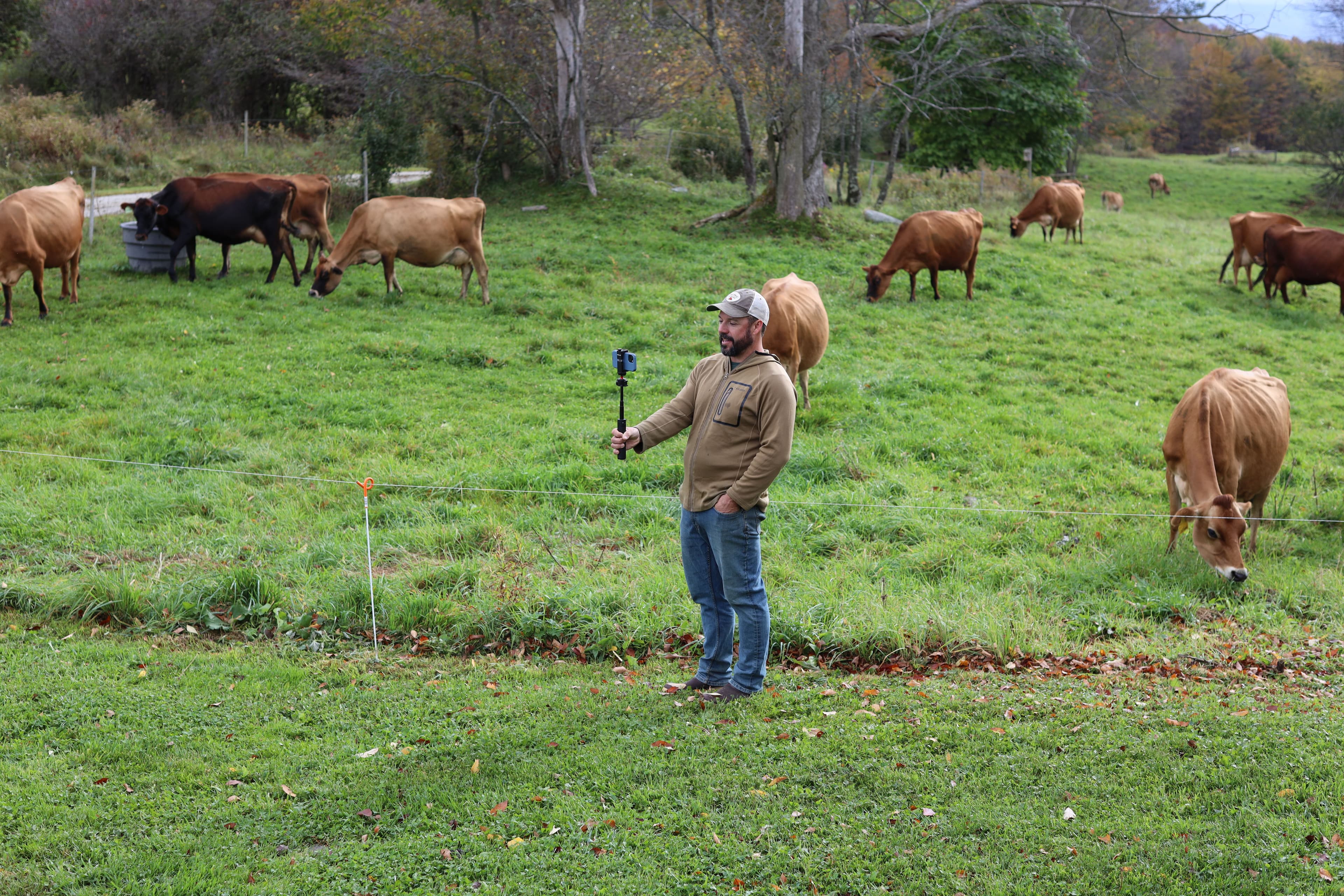  Vermont farmer Tyler Webb holds a camera as organic dairy cows graze in the background.