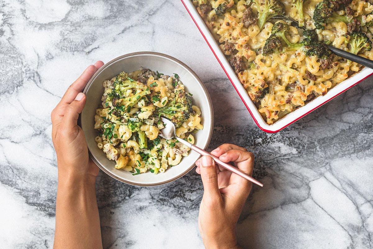 Baked Cheesy pasta in a bowl next to a pan of baked cheesy pasta.