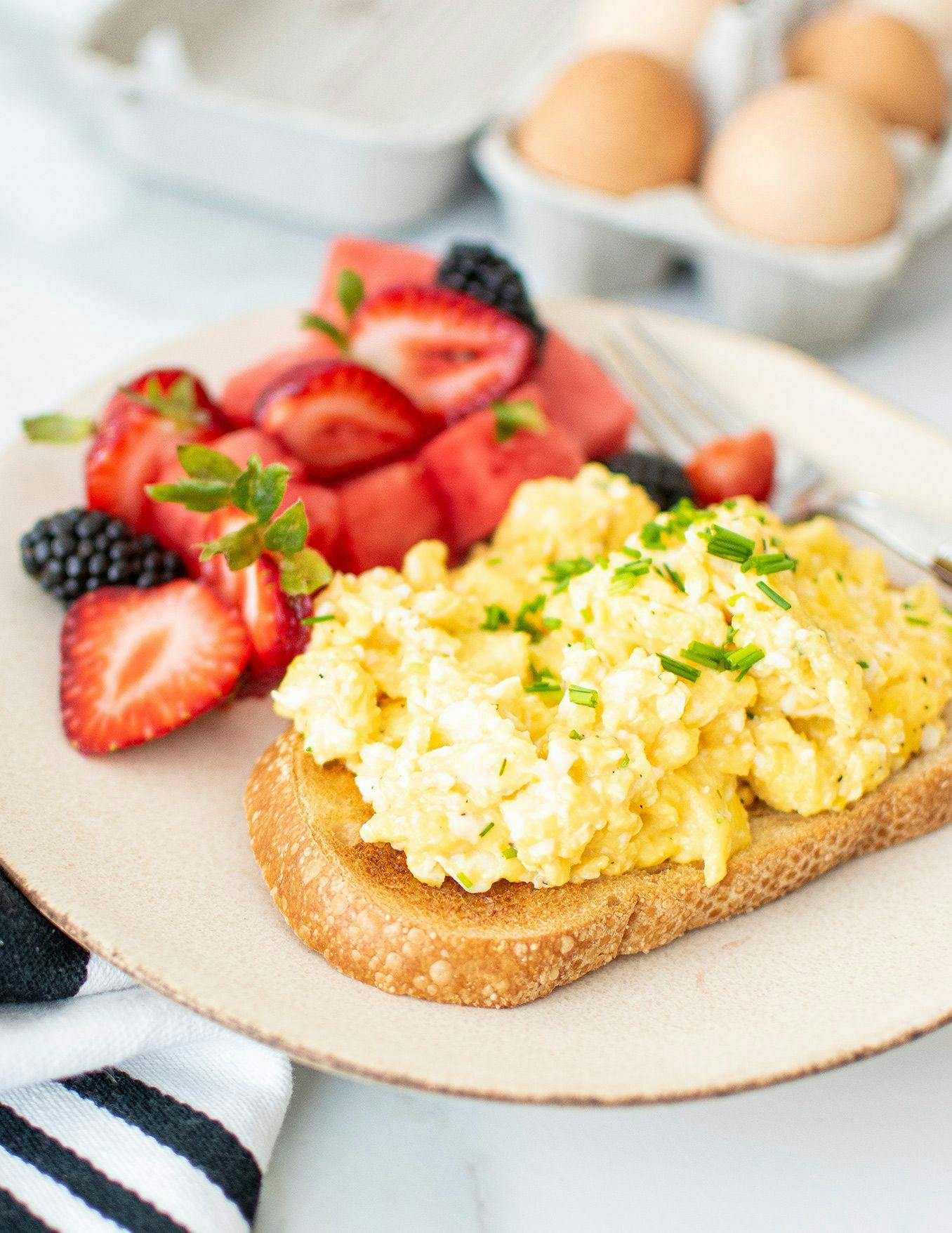 Fluffy eggs on toast next to fruits.