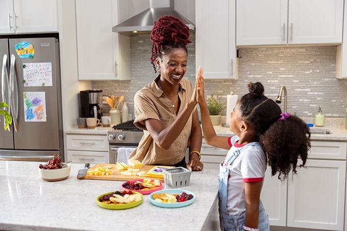 Mother and child high fiving and eating fruit and cheese.